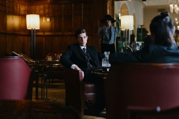 Young man in a dark suit sitting in a vintage lounge, illustrating romanticized experiences people have not lived.