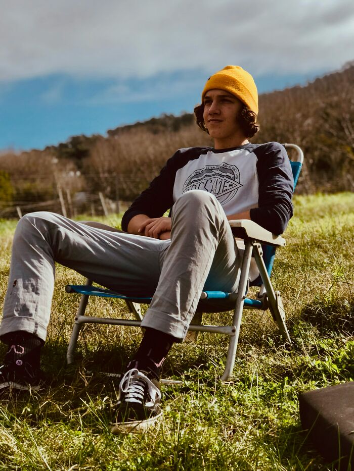 Young man wearing a yellow beanie relaxing outdoors on a chair, enjoying life hacks and common knowledge tips.