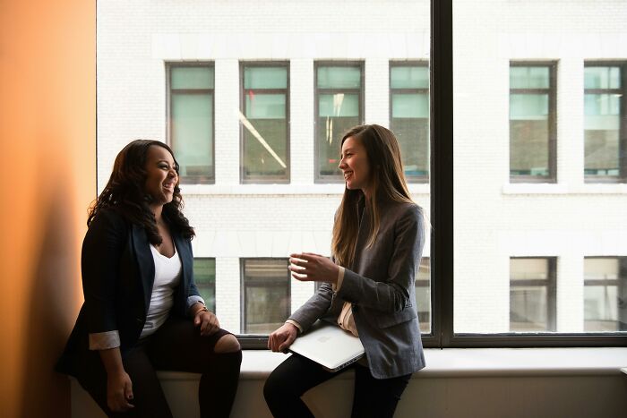 Two women sharing life hacks and tips in a bright office setting, discussing common knowledge and practical advice.