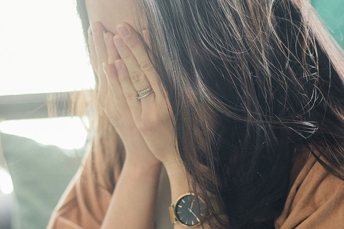 Woman covering her face with hands, wearing a watch and rings, representing former cult members sharing their experiences.