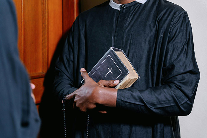 Man in black robe holding a Bible and rosary beads, symbolizing experiences shared by former cult members.