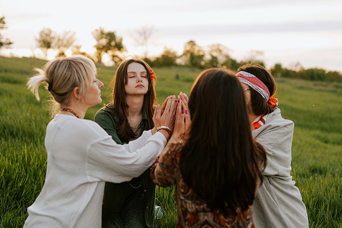 Four women outdoors in a grassy field participating in a group ritual, illustrating former cult members' experiences.