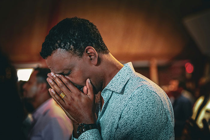Man with hands clasped near face in a crowded room, reflecting the experience of former cult members realizing their situation.