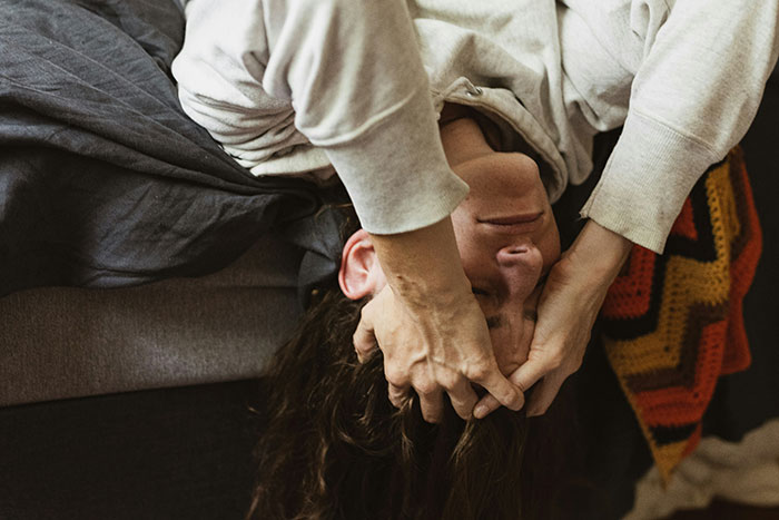 Person lying down with hands on head, showing distress, illustrating experiences of former cult members.