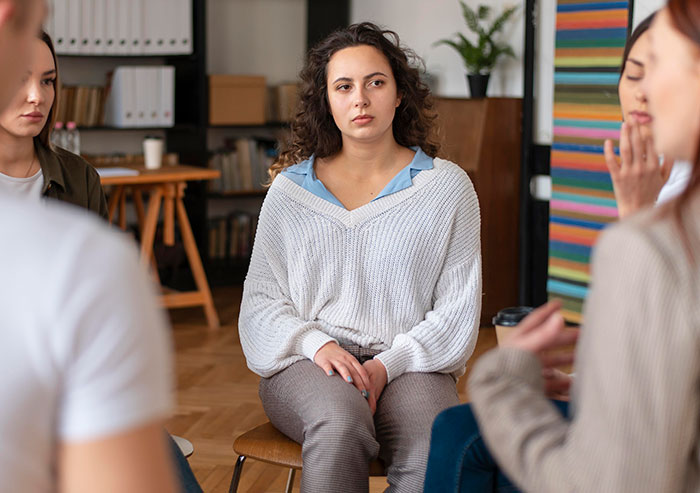 Young woman listening during a group therapy session with former cult members sharing their experiences.