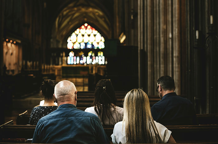 People sitting in a dimly lit church with stained glass windows, reflecting on experiences as former cult members.