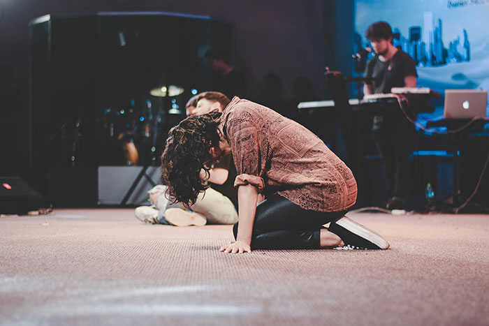 Person kneeling on the floor in a dimly lit room, representing former cult members reflecting on their experiences.