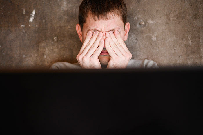 Man rubbing his eyes in frustration while reflecting on experiences as a former cult member in dimly lit room