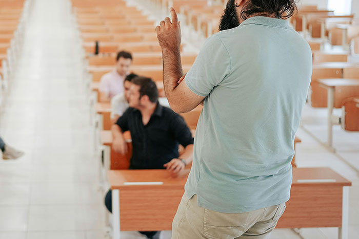 Man with beard teaching a small group in a classroom setting, illustrating former cult members' shared experiences.