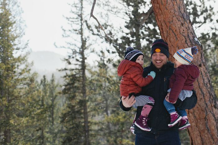 Man holding two children outdoors in winter forest, reflecting on disturbing confessions shared casually.
