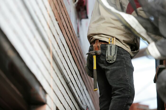 Construction worker with hammer and tool belt at a brick wall, symbolizing casual disturbing confessions shared on site.