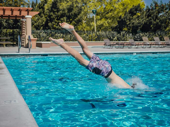 Person diving into a clear swimming pool on a sunny day, highlighting healthy activities to prevent tinnitus on a daily basis.