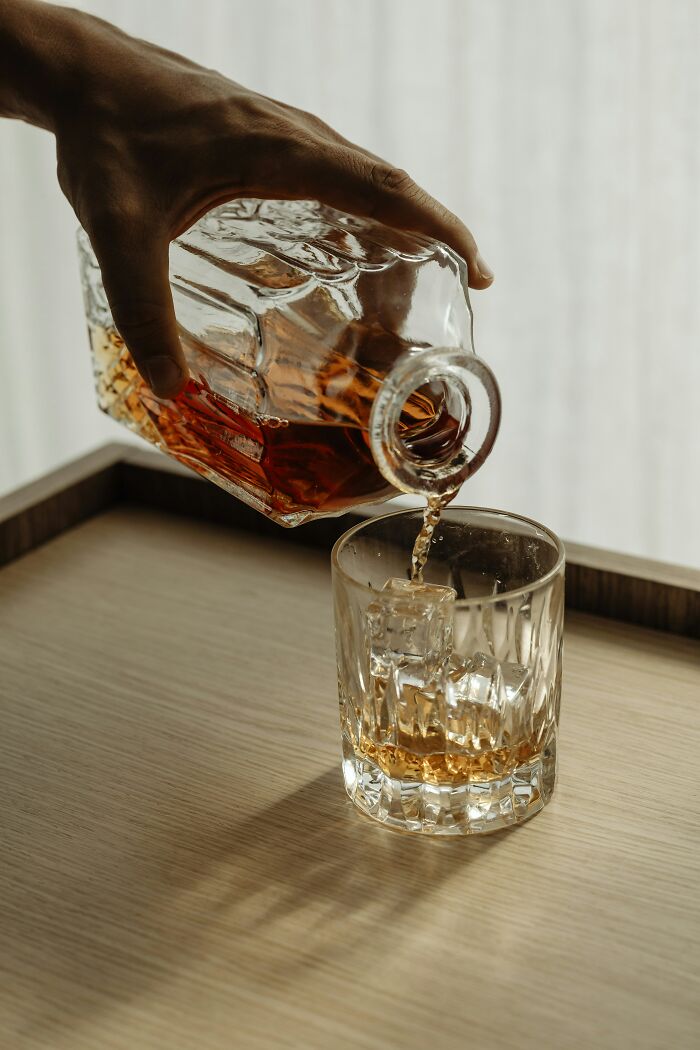 Hand pouring whiskey from a glass decanter into a glass with ice, illustrating habits linked to tinnitus daily.
