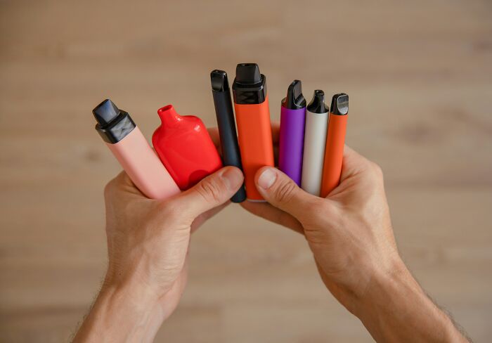 Hands holding various colorful vaping devices, illustrating habits that may cause tinnitus on a daily basis.