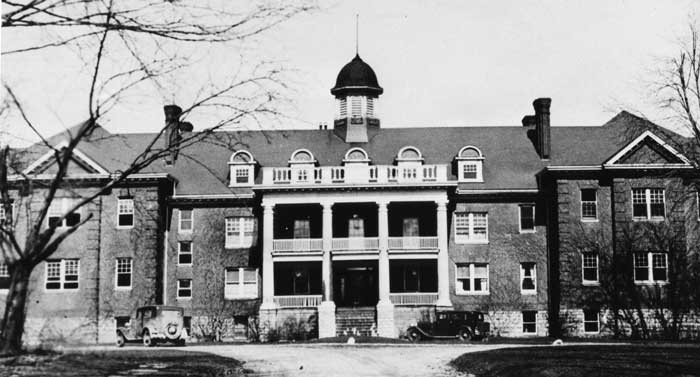 Black and white photo of an old large brick family house representing dark family secrets revealed in adulthood.