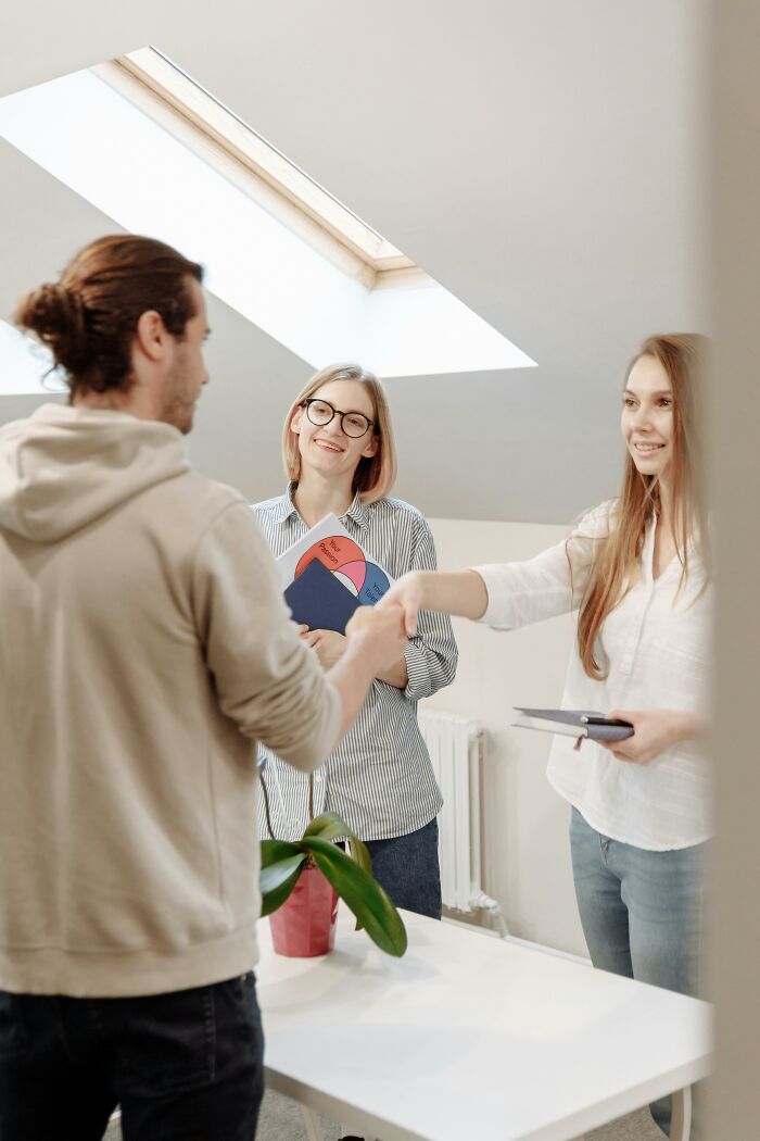 Two women supporting women shake hands with a man during a friendly meeting in a bright office setting.