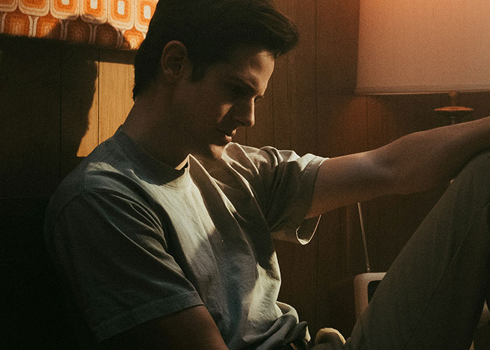 Young man sitting alone in dim light, appearing thoughtful and regretful about cheating partners and exposed secrets.