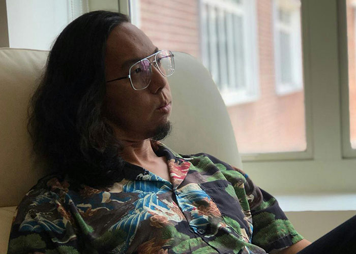 Man with glasses and long hair sitting thoughtfully on a couch reflecting on cheating partners and relationship betrayal.