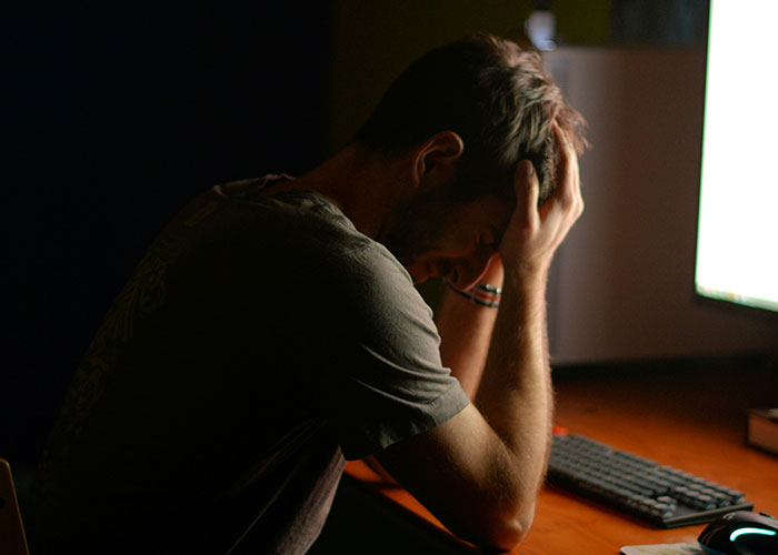 Man sitting in front of computer holding his head, showing stress and emotions related to exposing cheating partners.