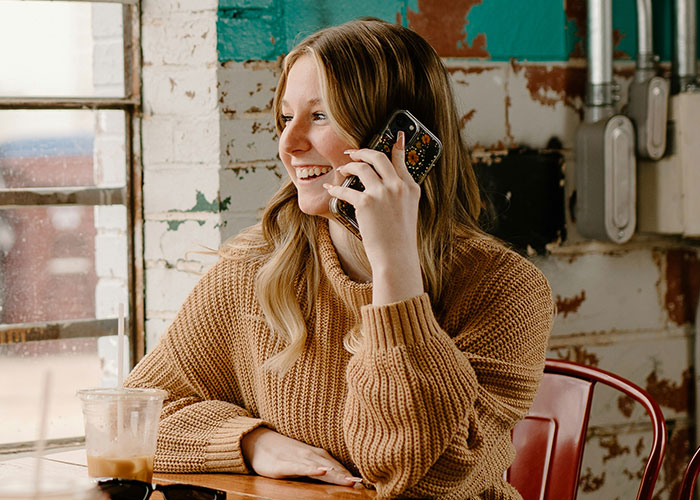 Young woman in a cozy sweater smiling while talking on the phone, symbolizing how people exposed cheating partners.