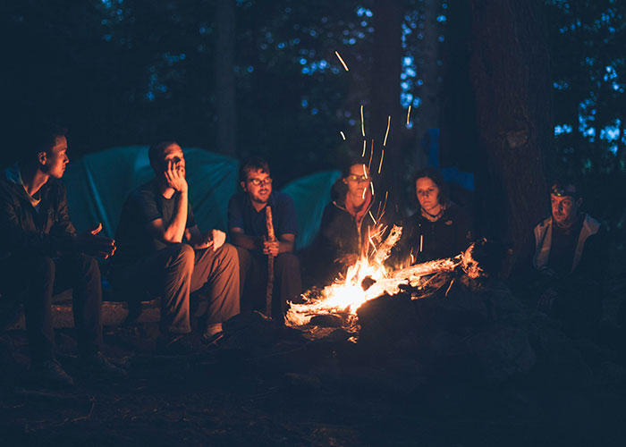 Group of people sitting around a campfire at night sharing stories about exposing cheating partners and revealing secrets.