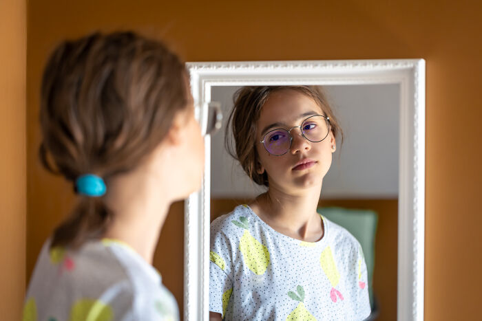 Teenage girl looking thoughtfully at her reflection in a mirror, evoking spooky tales of resurrection and time travel feelings.