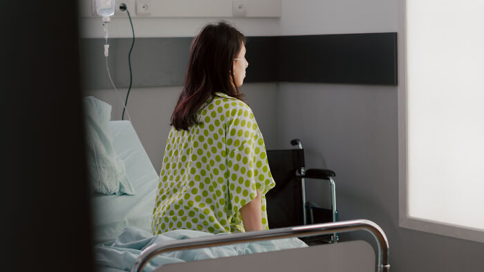 Woman in hospital gown sitting on a bed, reflecting on eerie stories of passing away and being resurrected.