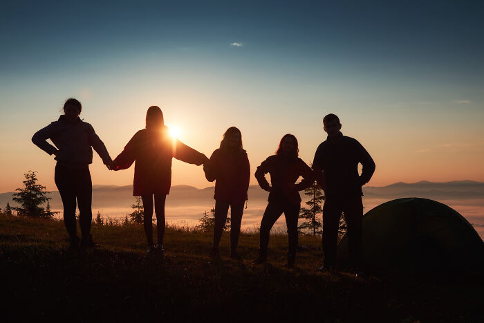 Silhouettes of five people holding hands at sunset in a spooky setting, evoking tales of passing away and resurrection.