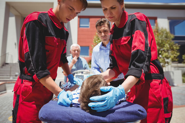 Paramedics in red uniforms performing emergency resuscitation on a child outdoors, capturing spooky tales of resurrection.