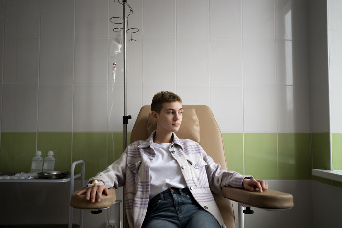 Young person sitting in a hospital chair receiving IV treatment, evoking spooky tales of people passing away and resurrection.