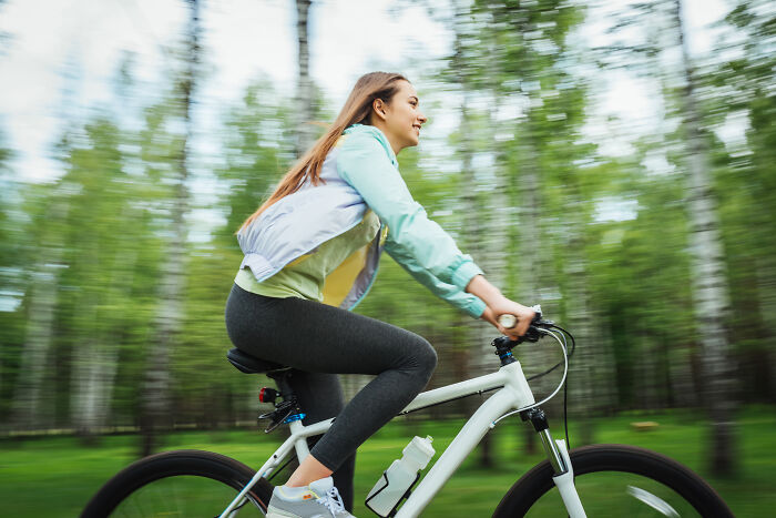 Young woman riding a bike through a forest, evoking a feeling of time travel and spooky tales of resurrection.