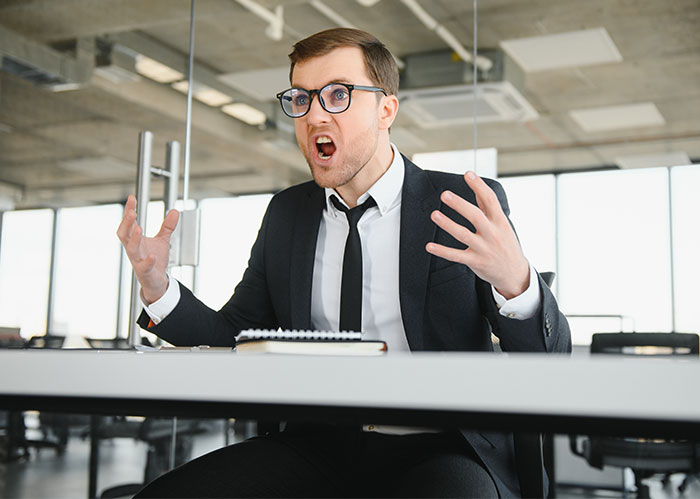 Angry manager displaying hostile workplace behavior during a tense office meeting in a modern workspace.