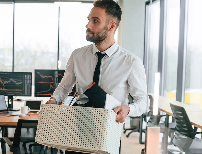 Man in office carrying box of belongings after manager created a hostile workplace environment and faced consequences.