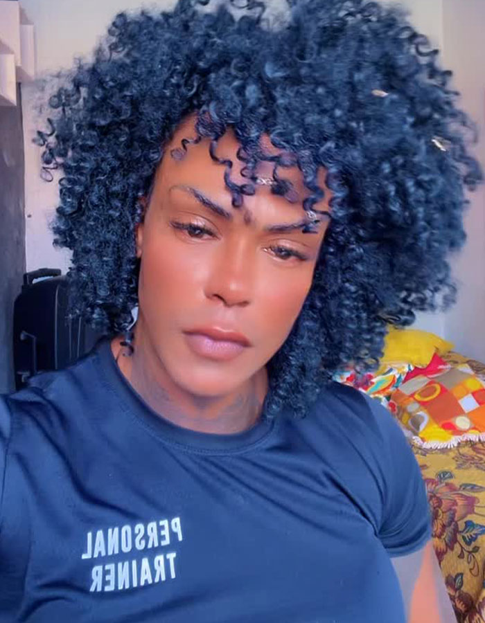 Person with curly hair wearing a personal trainer shirt, related to couple convinced cis woman is trans gym bathroom incident.