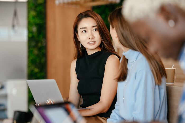 Young woman using a laptop and discussing real-life cheat codes with colleagues in a modern office setting.