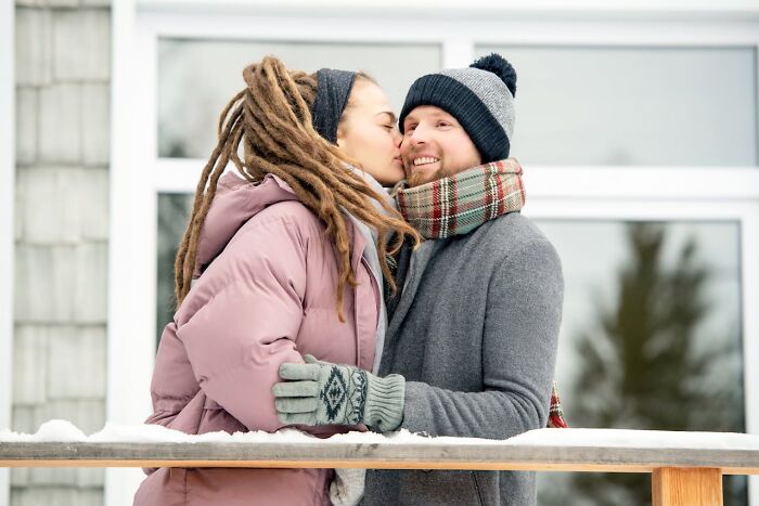 A couple dressed warmly in winter clothes sharing a tender moment outdoors with snow, capturing new facts today I learned.