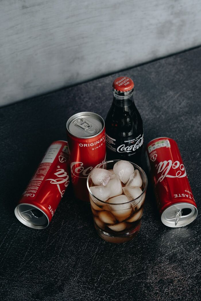 Cans and bottle of Coca-Cola with a glass of ice on a dark surface representing restaurant food beverages.