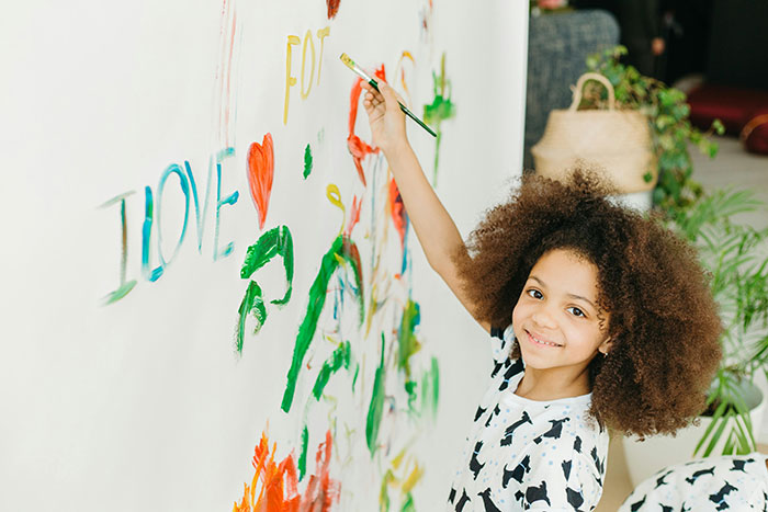 Young girl painting a colorful mural on a wall, symbolizing family dynamics and sibling relationships.