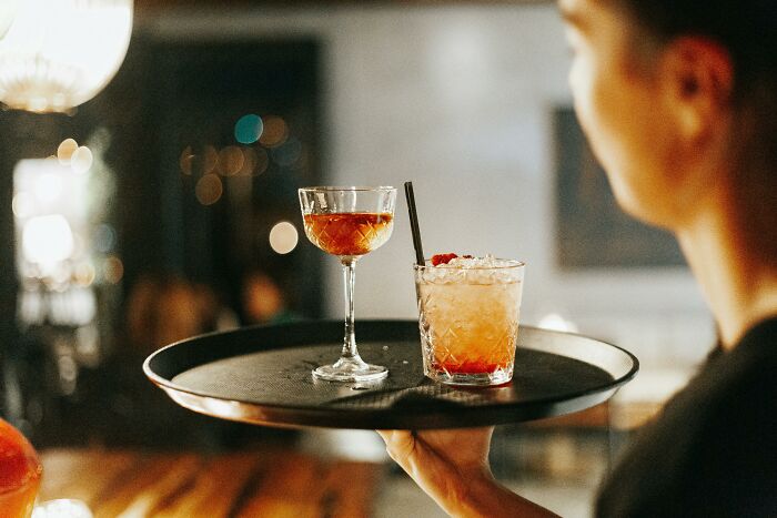 Bartender carrying a tray with two mixed drinks, showcasing the bartender job beyond just pouring drinks.