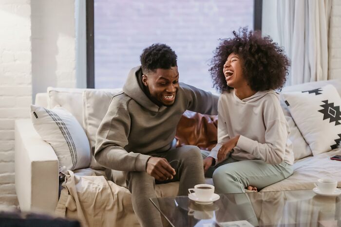 Two people laughing together on a couch, sharing moments of life advice in a bright, cozy living room setting.