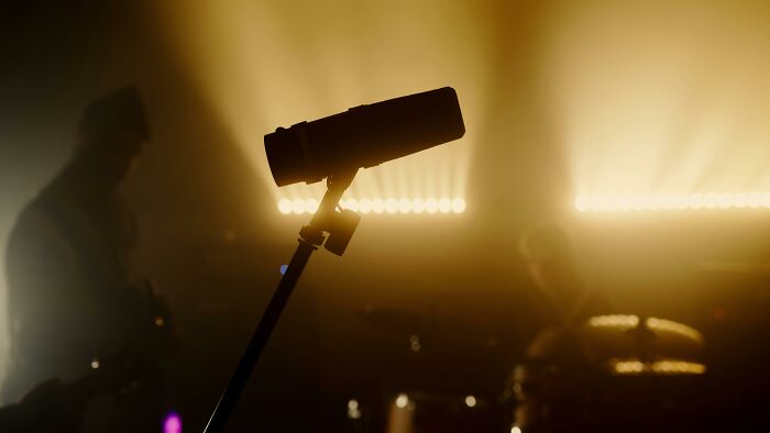 Microphone on stage with backlit musicians in the background, capturing lyrics of popular songs sung in the shower. Microphone on stage with backlit musicians in the background, capturing lyrics of popular songs sung in the shower.