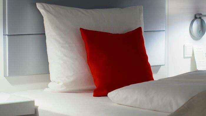 Close-up of a white bed with a red pillow, illustrating unexpected discoveries by tech guys fixing customer computers.