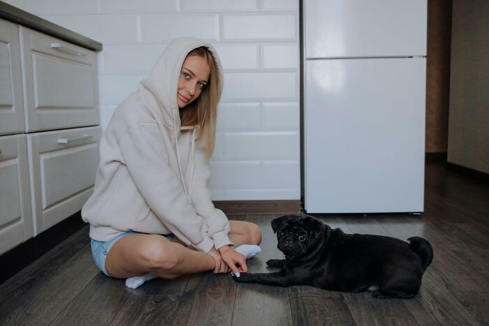 Young woman in a hoodie sitting on the floor with her black pug, illustrating mind-boggling beliefs smart people hold.