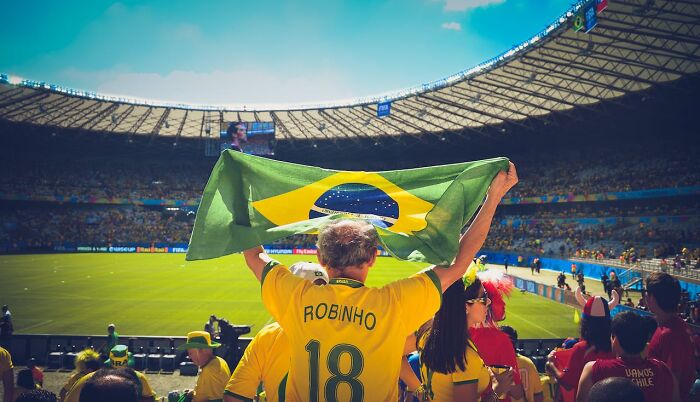 Brazil soccer fan holding national flag at stadium, capturing a moment tied to national stereotypes humor.