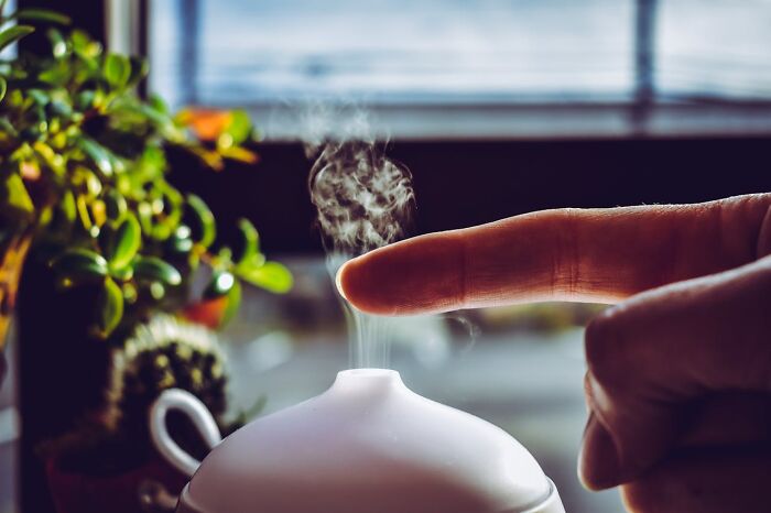 A person lazily touching the steam from a diffuser, illustrating one of the most excessively lazy things done indoors.