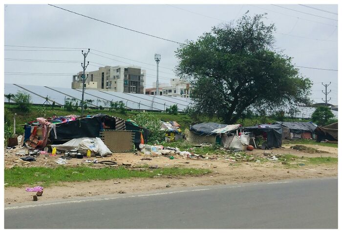 Informal outdoor shelters made from tarps and found materials near a road, highlighting out-of-touch people shamed online.