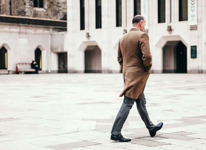 Man walking alone in an urban plaza wearing a coat, representing harshest pieces of when life gives you lemons advice.