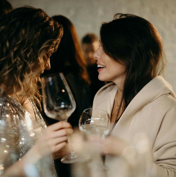 Two women holding wine glasses, smiling and talking at a social event about people who called off their wedding.
