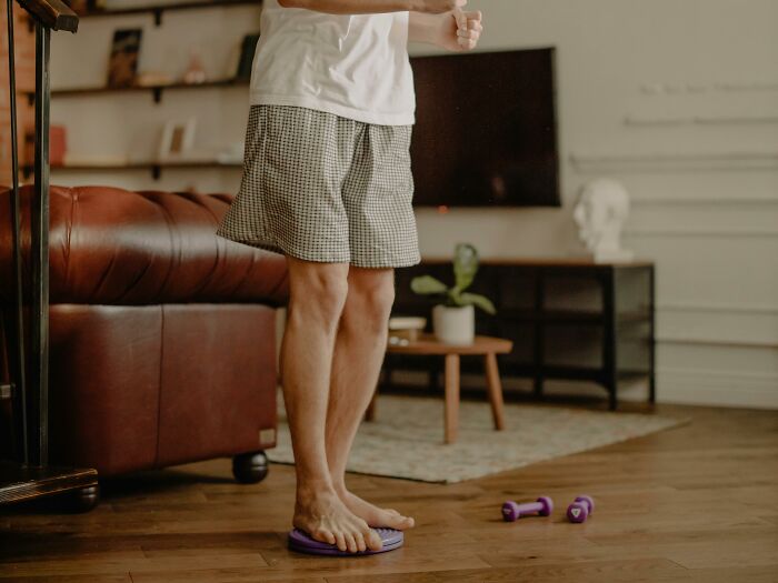 Person in shorts balancing on a purple disc in a living room, showing a funny and weird activity at home.