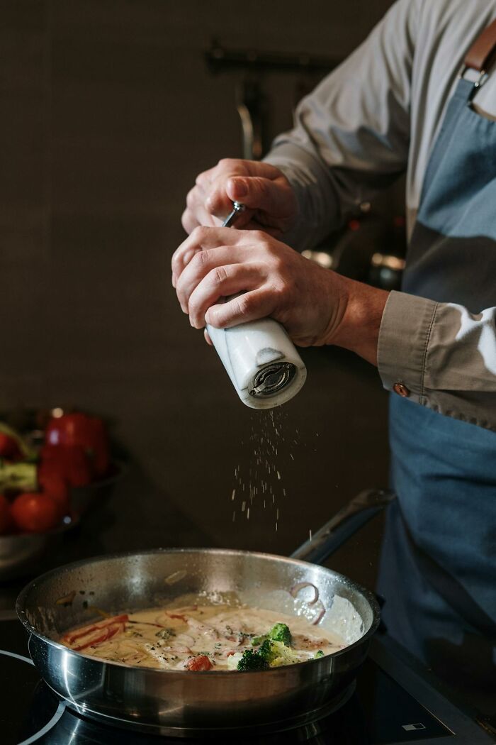 Person seasoning a creamy vegetable dish in a pan, showing an improvement that enhanced quality of life significantly